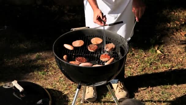 Человек готовит гамбургеры на барбекю — стоковое видео