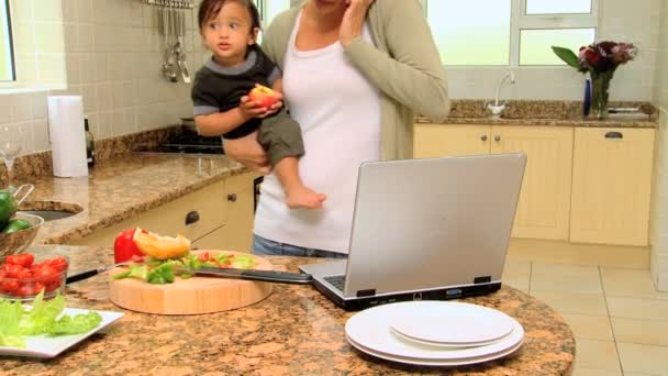 Madre joven en la cocina afrontando el teléfono portátil y el bebé — Vídeo de stock