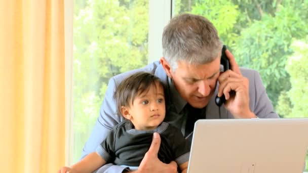 Man talar i telefonen medan hans baby fidgeting på hans knä — Stockvideo