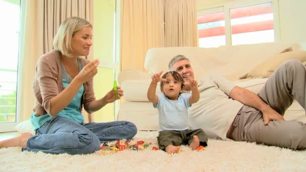 Мама надувает пузырьки для ребенка и мужа на ковре — стоковое видео