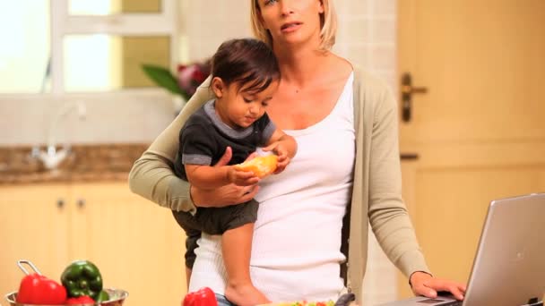 Trött mamma i köket håller baby och arbetar med laptop — Stockvideo
