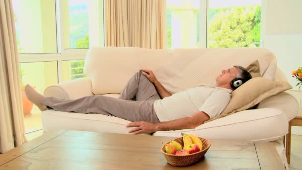 Man lying on sofa enjoying music with headphones — Stock Video