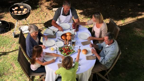 Семья разбирает столовые приборы за садовым столом перед едой — стоковое видео