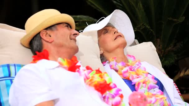 Зрелая пара с гирляндами, сидящая и улыбающаяся на солнце — стоковое видео