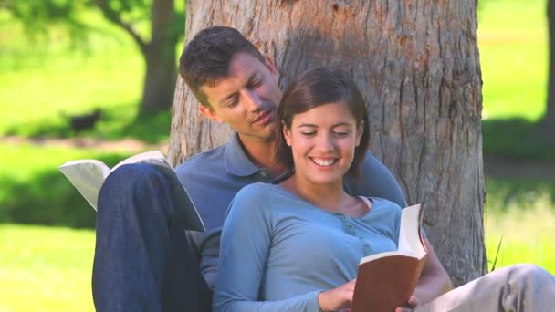 Jovem casal lendo livros sob uma árvore — Vídeo de Stock