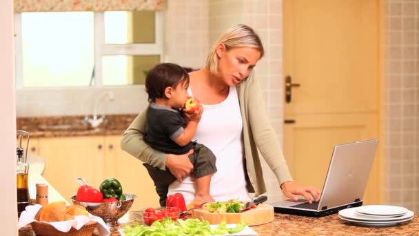 Madre affrontare il bambino durante la cottura e l'utilizzo di un computer portatile — Video Stock