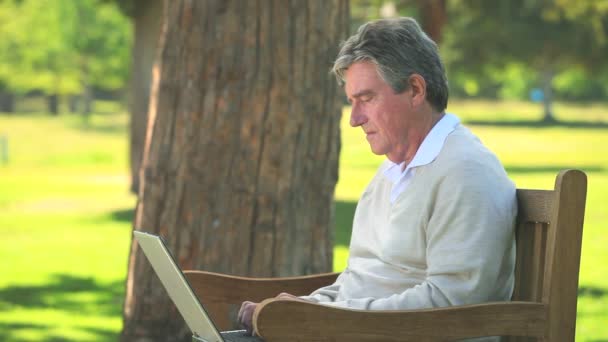 Elderly man using his laptop on a bench — Stock Video