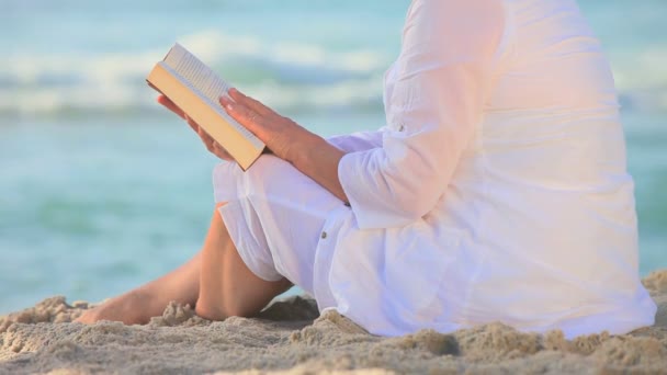 Reife Frau sitzt lesen auf einem Strand — Stockvideo