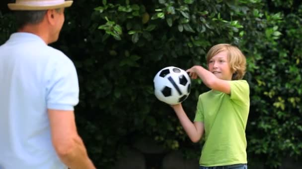 Pai e filho brincando com uma bola de futebol no jardim — Vídeo de Stock