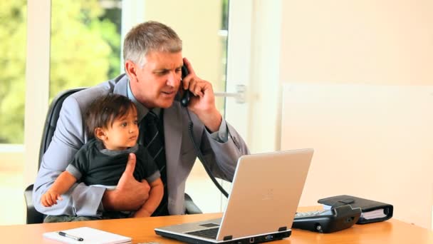 Man bedrijf baby en antwoordende telefoon op Bureau — Stockvideo