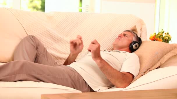 Man lying on sofa listening to music with headphones — Stock Video