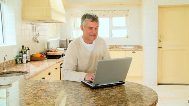 Mature man using a laptop in the kitchen — Stock Video