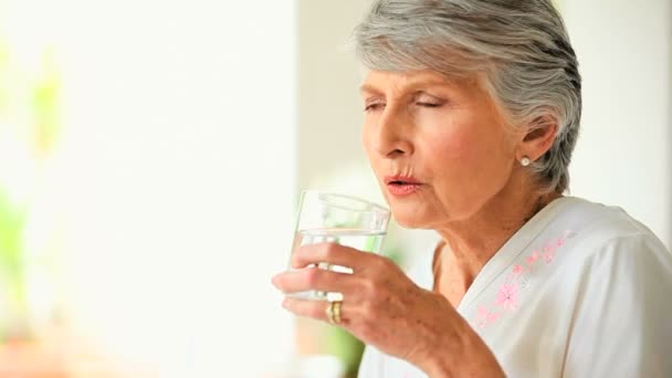 Зрелая женщина потягивает стакан воды — стоковое видео