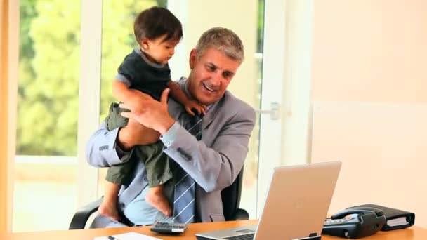 彼の腕で彼の息子を保持しながら、デスクで働くビジネスマン — ストック動画