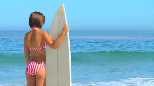 Mujer sosteniendo su tabla de surf mirando al mar — Vídeo de stock