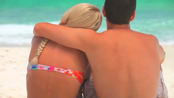 Dulce pareja sentada abrazándose en una playa — Vídeo de stock
