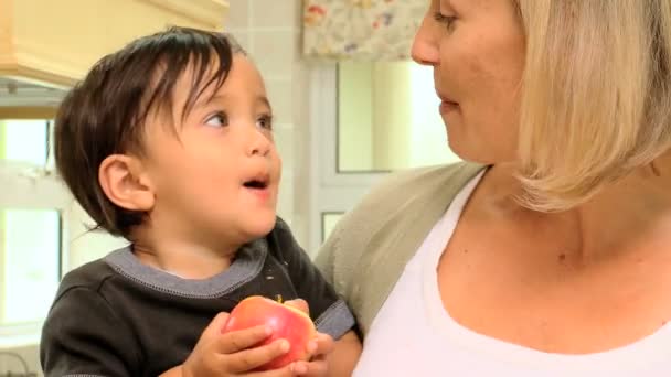 Baby in moeders armen een rode appel eten — Stockvideo