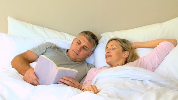 Hombre leyendo un libro en la cama con su esposa — Vídeo de stock