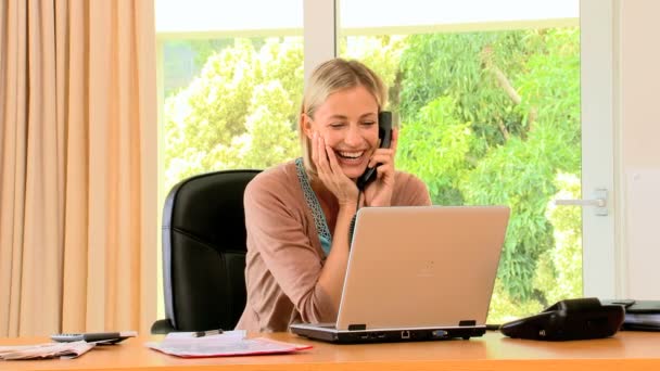 Young woman working on a laptop and laughing on phone — Stock Video