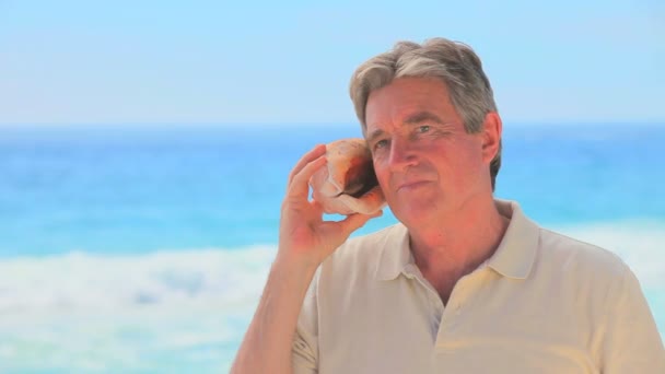 Mature man listening to a shell — Stock Video