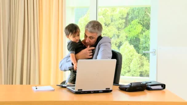 Бизнесмен держит малыша и работает — стоковое видео