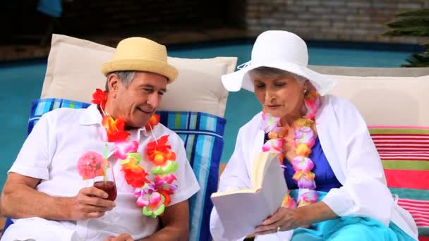 Pareja con guirnaldas junto a la piscina riéndose por un libro — Vídeos de Stock