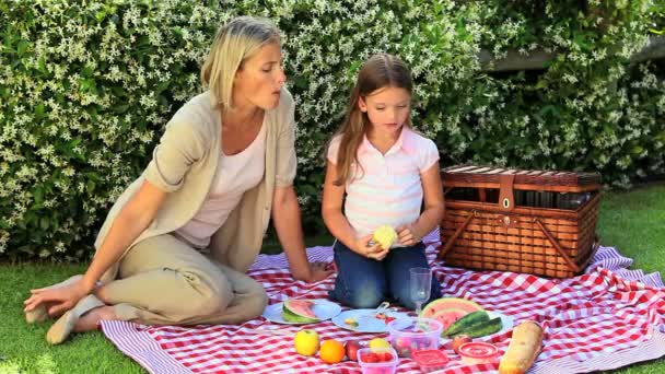 Mujer joven y su hija comiendo frutas en el jardín — Vídeo de stock