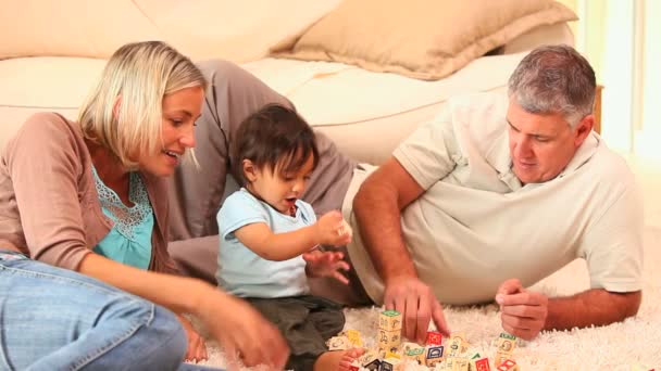 Родители на ковре показывают своему ребенку, как играть с блоками — стоковое видео
