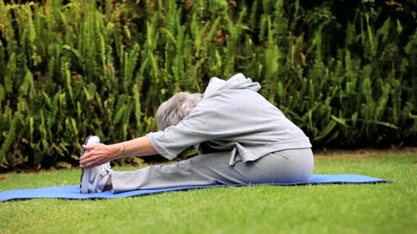 Mogen kvinna göra stretchingövningar på gräsmattan — Stockvideo
