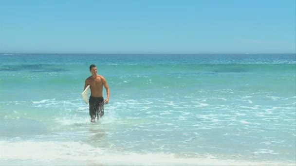 Hombre guapo saliendo del agua después de surfear — Vídeos de Stock