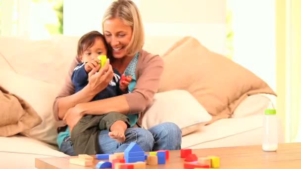 赤ちゃんと一緒に遊んでソファーで若い母親 — ストック動画