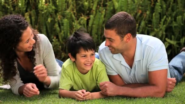 Kleine jongen liggen op het gras chatten met zijn ouders — Stockvideo
