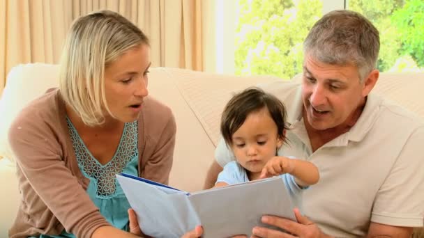 Ouders met baby kijken naar boek — Stockvideo