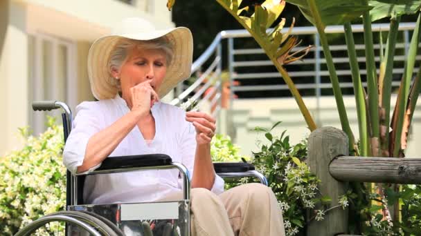 Mulher em uma cadeira de rodas cheirando uma flor — Vídeo de Stock