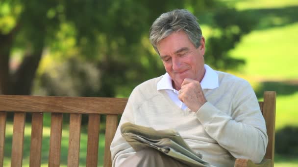 Mature man reading a newspaper on a bench — Stock Video