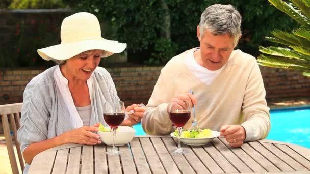 Mature couple laughing over lunch by a swimming pool — Stock Video