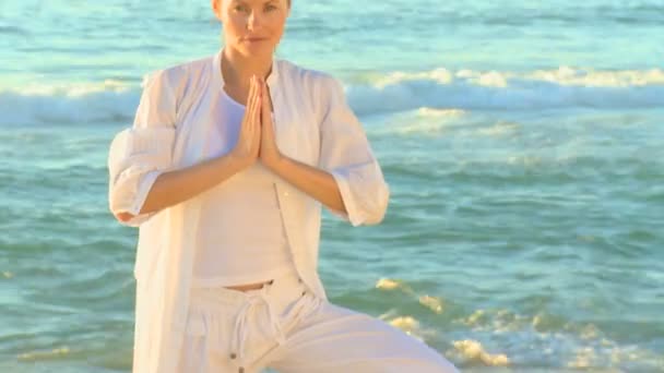 Blond kvinna i vitt som gör yoga på en strand — Stockvideo