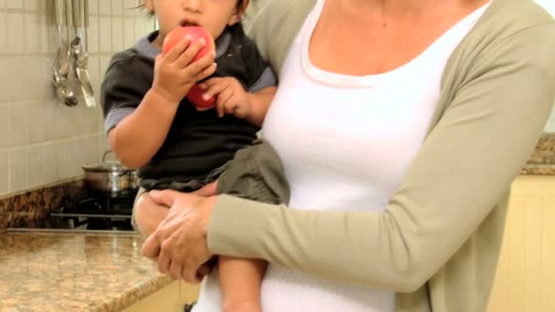 Mother in kitchen holding baby with red apple — Stock Video