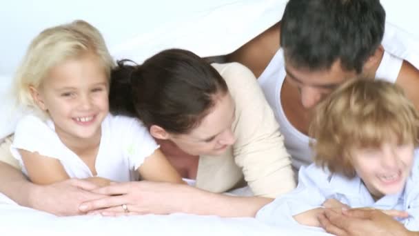 Familia feliz teniendo una pelea de almohadas en una cama — Vídeo de stock