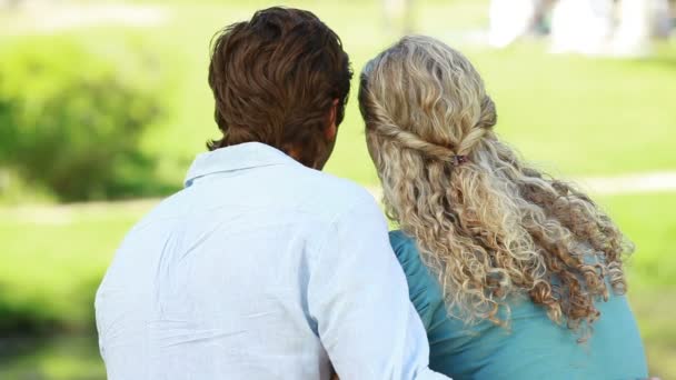 Un hombre y una mujer se sientan en el parque abrazados mientras se besan — Vídeos de Stock