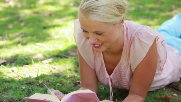 Una mujer relajándose en la hierba mientras lee un libro — Vídeo de stock