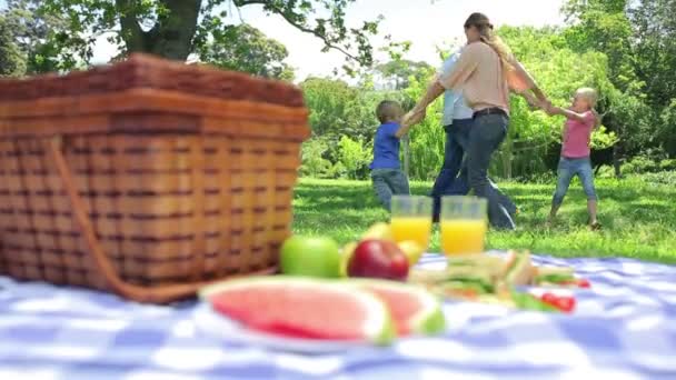 Familie dansen in een cirlcle op de achtergrond met een schotel op een picknickmand op de voorgrond — Stockvideo