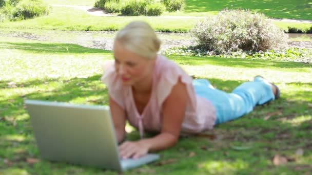 De camera verlegt focus van het park naar een vrouw op haar laptop als ze leest — Stockvideo