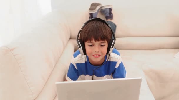 Niño usando un ordenador portátil está usando auriculares — Vídeos de Stock