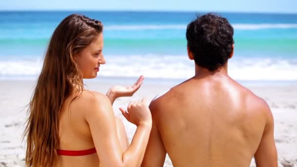 Брюнетка намазывает солнцезащитный крем на своего парня — стоковое видео