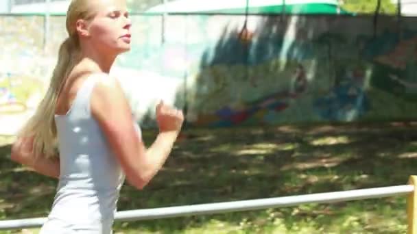 Eine bewegende Seitenansicht einer Frau, die eine Straße hinunterjoggt und sich umsieht — Stockvideo