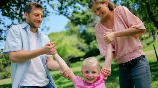 Dois pais sorriem enquanto balançam sua filha para frente e para trás por seus braços brincando — Vídeo de Stock