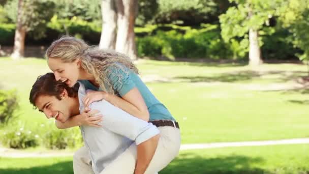 Un uomo dà alla sua ragazza un piggy-back mentre guardano la fotocamera e sorridono — Video Stock