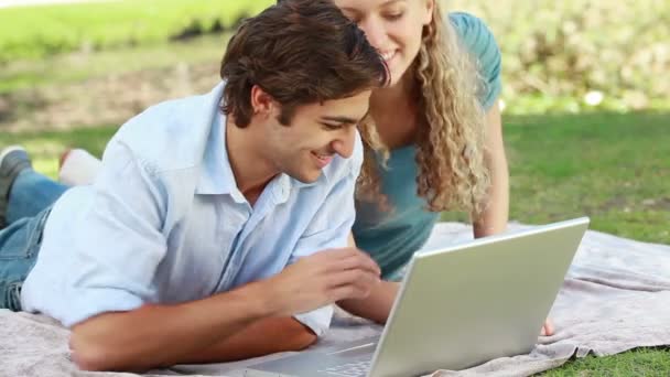 Un uomo giace con un computer portatile mentre la sua ragazza si trova accanto a lui e guardano nella fotocamera — Video Stock