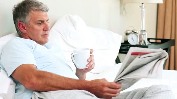 Homem lendo um jornal em sua cama — Vídeo de Stock